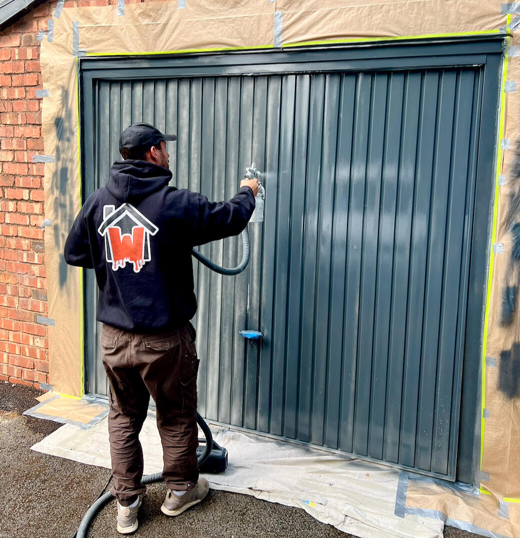Garage door spray painting service applying a smooth dark grey finish to an exterior metal garage door with professional masking and preparation.